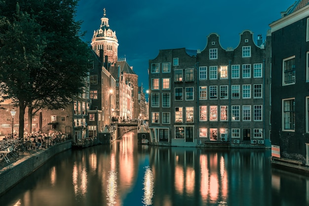 Quartiere a luci rosse di notte De Wallen, canale Oudezijds Voorburgwal, ponte, Basilica di San Nicola e il suo riflesso speculare, Amsterdam, Olanda, Paesi Bassi.