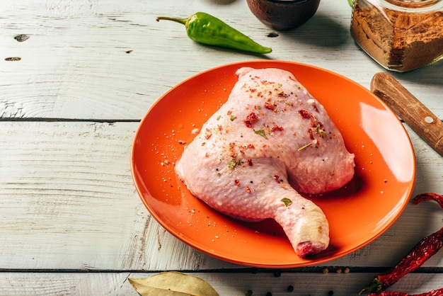 Quarto di coscia di pollo sul piatto arancione sulla superficie in legno con spezie diverse