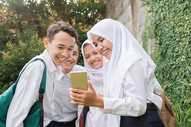 Quattro adolescenti in uniforme della scuola media che usano e guardano i cellulari