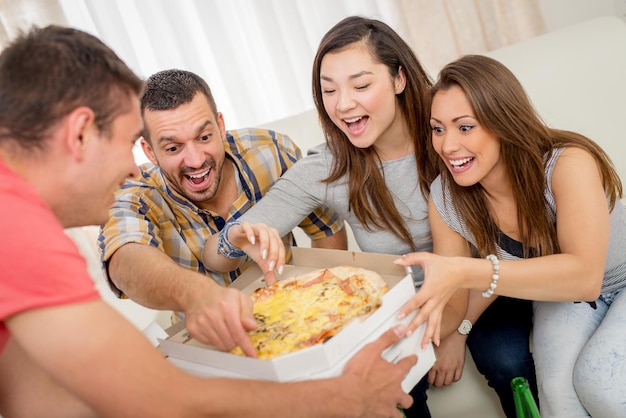 Quattro amici allegri che si godono la pizza insieme a casa. Messa a fuoco selettiva.