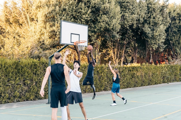 Quattro amici di diverse etnie giocano a basket in uno spazio aperto durante il tramonto