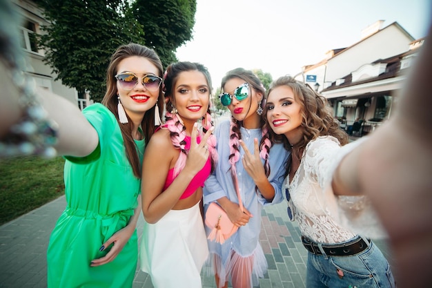 Quattro belle e alla moda migliori amiche con gli occhiali, in posa per i social network, lo stile di vita, trascorrono il tempo divertendosi. Donne in occhiali da sole dopo lo shopping e il salone di bellezza.