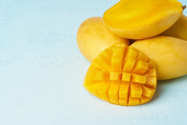Quattro frutti di mango interi sul tavolo blu brillante e tagliati a fette