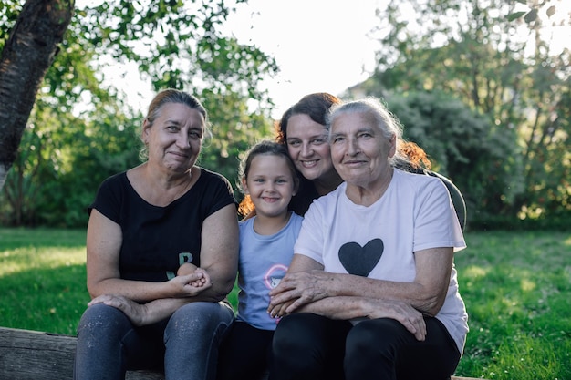 Quattro generazioni di donne di una famiglia seduta sul log all'esterno guardando la fotocamera sorridente durante il giorno con il verde sullo sfondo Trascorrere del tempo insieme e divertirsi