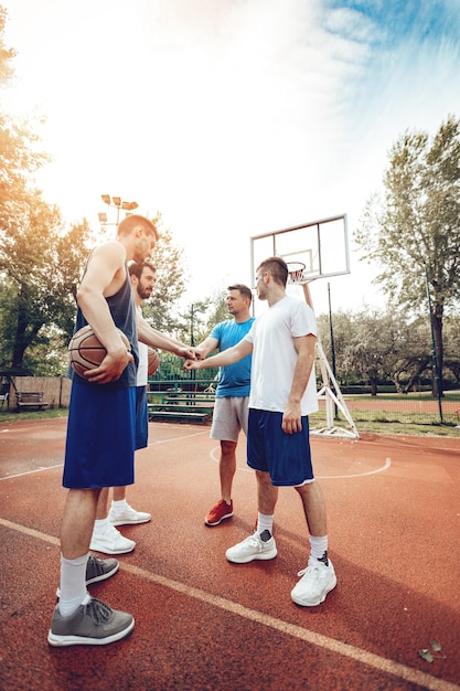 Quattro giocatori di basket che salutano lo sport prima dell'allenamento. Hanno colpito i pugni con il sorriso sulle labbra.