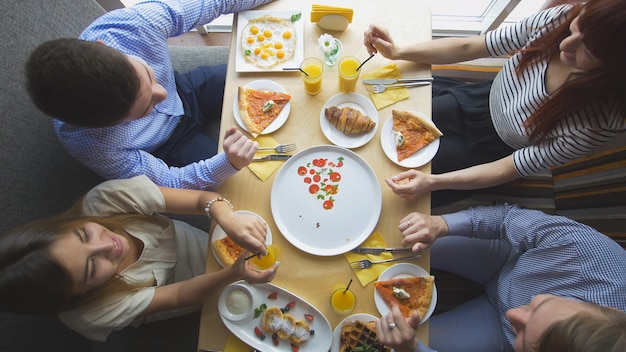 Quattro giovani amici seduti al bar e fanno colazione - pizza, succo di frutta, dessert, vista dall'alto