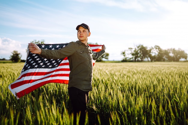 Quattro luglio. Uomo patriottico con la bandiera americana nazionale nel campo. Giovane uomo che sventola con orgoglio una bandiera americana. Giorno dell'Indipendenza.