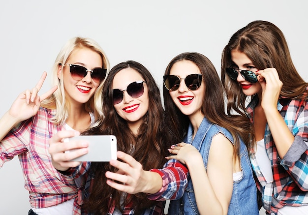 Quattro ragazze adolescenti felici con smartphone che prendono selfie