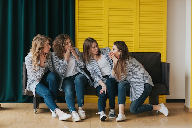 Quattro ragazze in camicie a righe, jeans e scarpe da ginnastica in posa sul divano. riprese in studio.