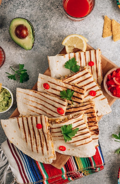 Quesadillas alla griglia su tavola di legno e con salsa e guacamole su sfondo di pietra Concetto di cucina messicana Impacco di quesadilla con pollo e mais Vista dall'alto