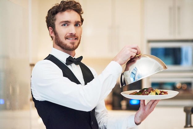 Questa è la nostra specialità Ritratto ritagliato di un bel giovane cameriere che tiene un piatto di cibo in un ristorante