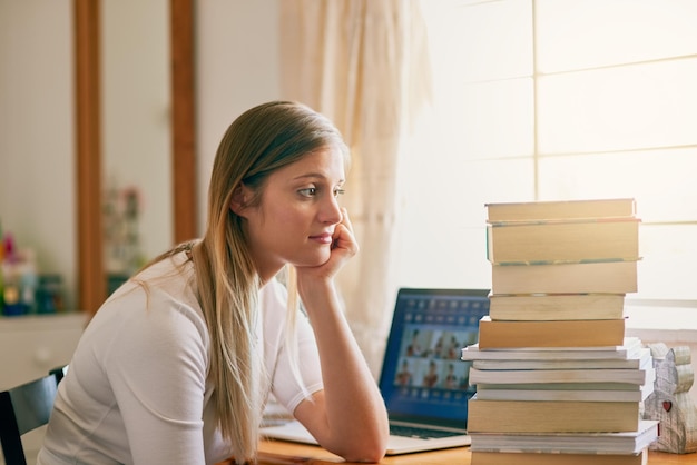 Questa è una quantità schiacciante di informazioni Inquadratura di una giovane donna che sembra sopraffatta dalla pila di libri sulla sua scrivania