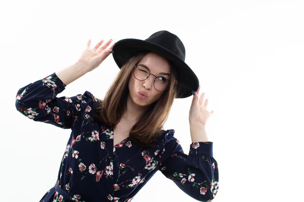 Questa elegante signora è vestita con un abito floreale fluido e un delicato cappello a tesa larga che incarna la bellezza e la semplicità della natura in un sereno ambiente da studio bianco