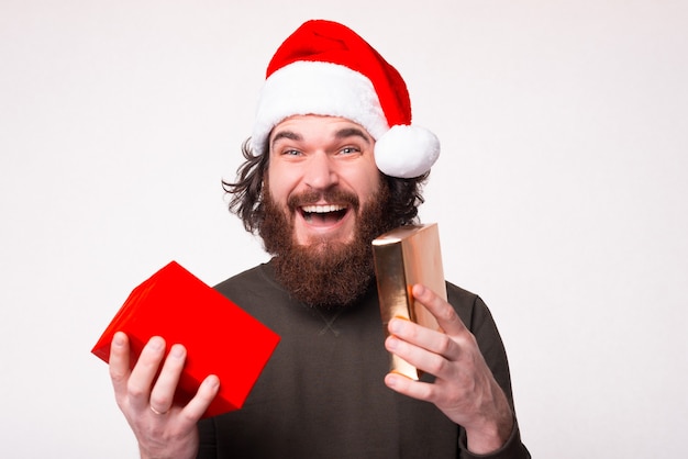 Questo è il regalo che ho voluto. L'uomo barbuto sorpreso che porta il cappello di natale sta tenendo una confezione regalo.