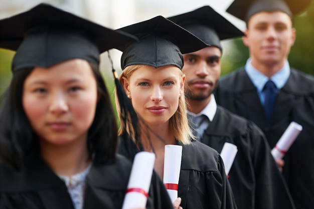 Questo è l'inizio di tutto ciò che vuoi Un gruppo di laureati in piedi in berretto e abito e con in mano i loro diplomi