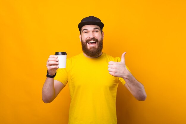 Questo è un buon caffè. Uomo felice con la barba che tiene tazza di caffè e che mostra il pollice in su