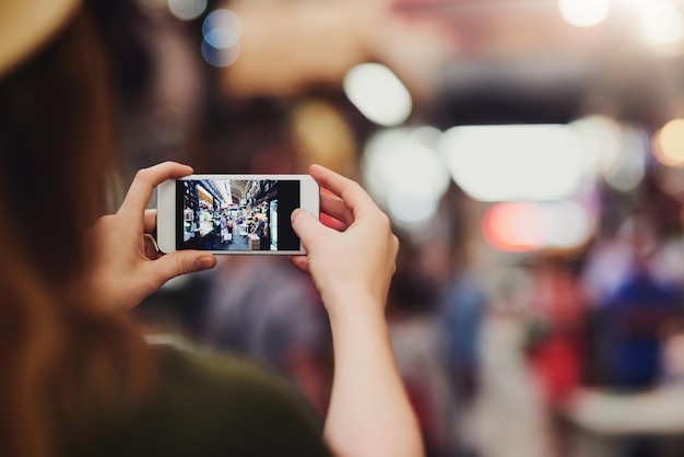 Questo sta per uscire a tutti i miei amici Foto da sopra la spalla di una donna irriconoscibile che scatta foto in un mercato affollato fuori durante il giorno