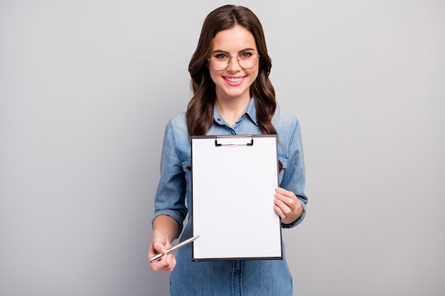 Qui! Foto di bella donna d'affari ondulata tenere appunti che mostra lo spazio del contratto per la registrazione dei dettagli indossare le specifiche jeans casual camicia di jeans isolato colore grigio