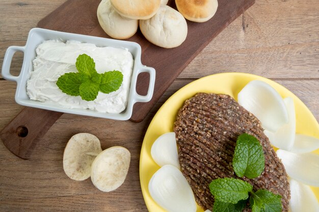 Quibe crudo con cipolla affettata, cagliata secca, pane pita e foglie di menta.