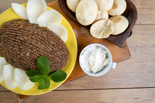 Quibe crudo con cipolla affettata, cagliata secca, pane pita e foglie di menta.