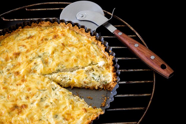 Quiche casalinga affettata con pollo, formaggio e cipolla verde e prezzemolo e coltello da pizza sul nero