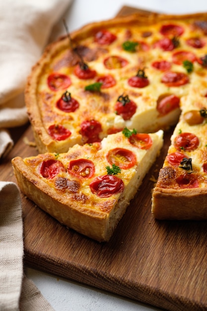 Quiche con pollo, pomodorini e formaggio. Torta francese aperta appetitosa. Piatto su una tavola di legno sul tavolo della cucina. Verticalmente.