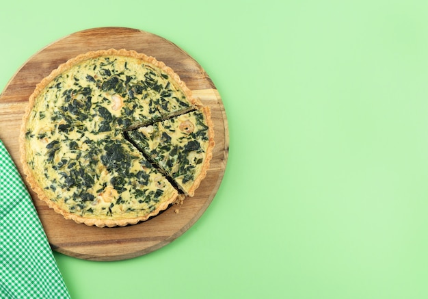 Quiche di verdure con porzione affettata su sfondo verde. Copia spazio.