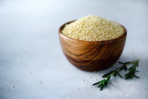 quinoa biologica cruda in ciotola di legno e rosmarino su grigio. Ingredienti alimentari sani Copia spazio