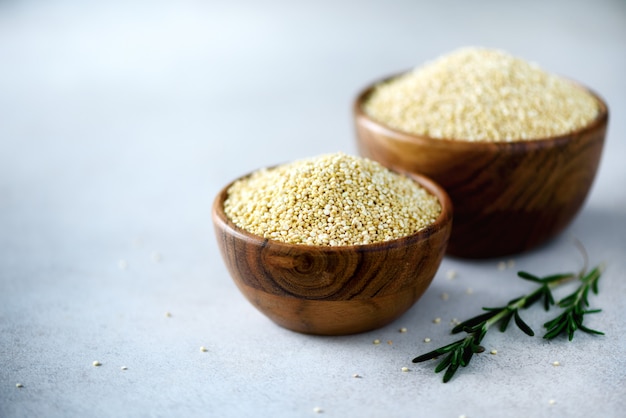 quinoa biologica cruda in ciotola di legno e rosmarino su grigio. Ingredienti alimentari sani Copia spazio