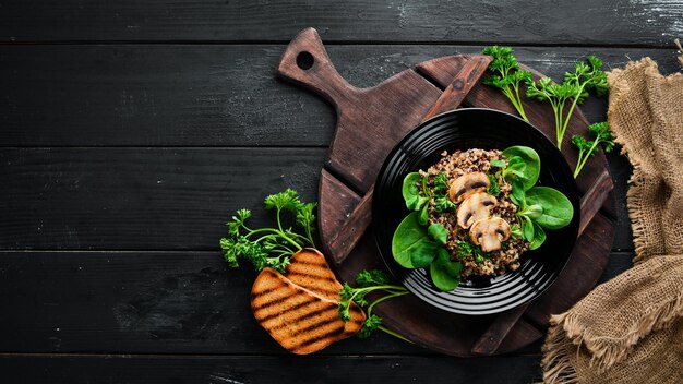 Quinoa con spinaci e funghi In un piatto nero su sfondo di legno Vista dall'alto Spazio libero per il testo Disposizione piatta