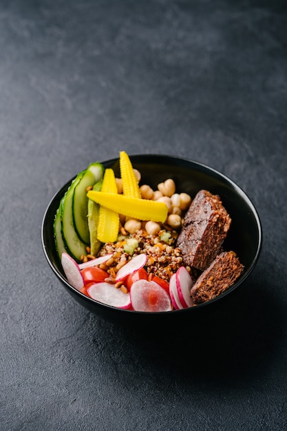 Quinoa con succosa cotoletta vegana, cetriolo, ravanello, mini mais e ceci su sfondo scuro