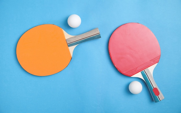 Racchette da ping pong e palline di plastica bianche su sfondo blu.