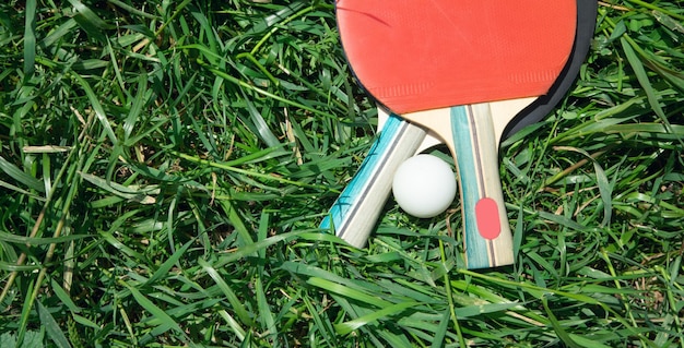 Racchette da ping pong e una palla di plastica bianca sullo sfondo dell'erba verde