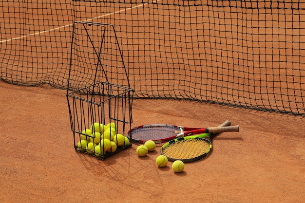 Racchette e cesto con palline da tennis su campo in terra battuta