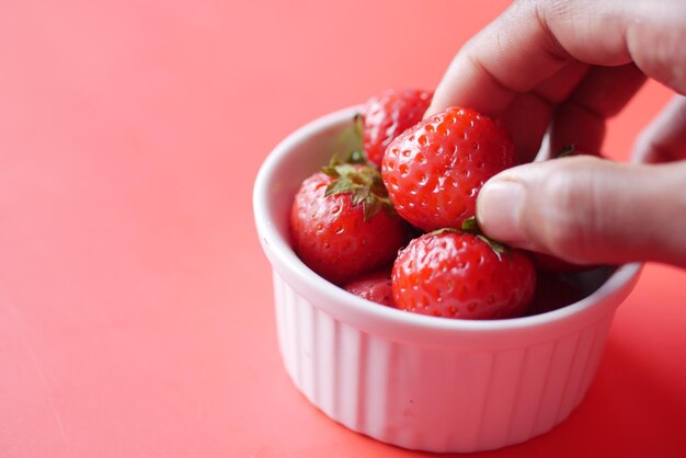 Raccogliere a mano le fragole rosse mature in una ciotola sul tavolo