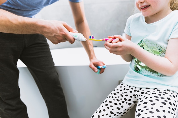 Raccolga il padre che mette il dentifricio sullo spazzolino da denti della figlia