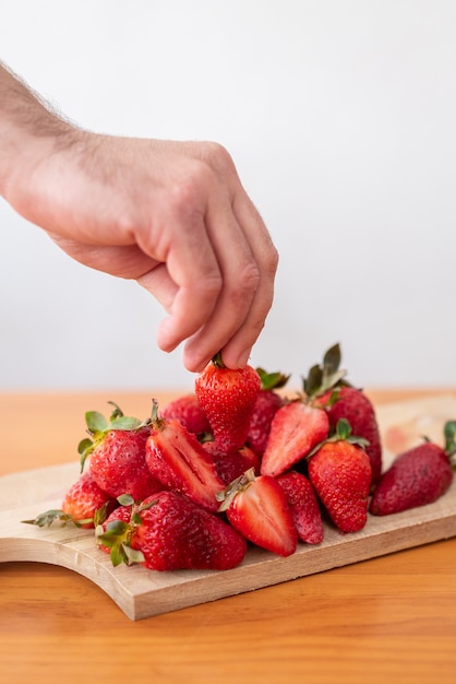 Raccolta a mano una fragola da un tagliere di legno.