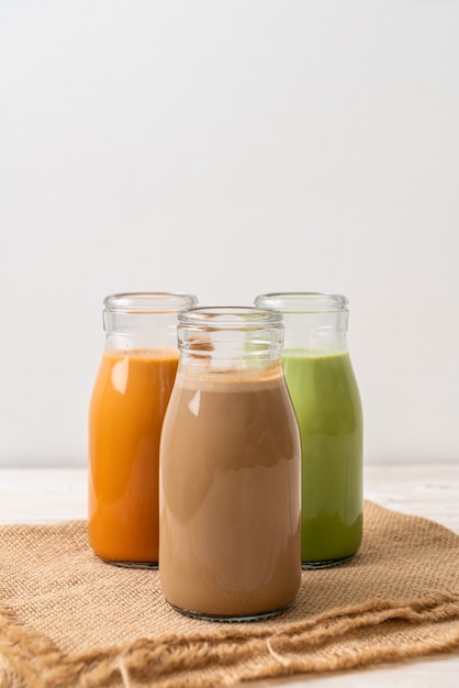 Raccolta di bevanda tè al latte tailandese, tè verde matcha latte e caffè in bottiglia su fondo di legno