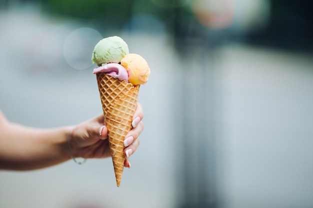 Raccolto della mano della donna che tiene delizioso gelato colorato con tre colori Primo piano di gustosi dolci appetitosi perfetti per la calura estiva durante la giornata di sole Vibrazioni estive e cibo dolce