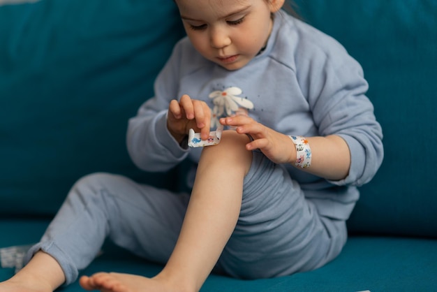 Raccolto di bambino bastone un cerotto sulla ferita sulle ginocchia Bambina bambino che indossa la colla blu con la toppa