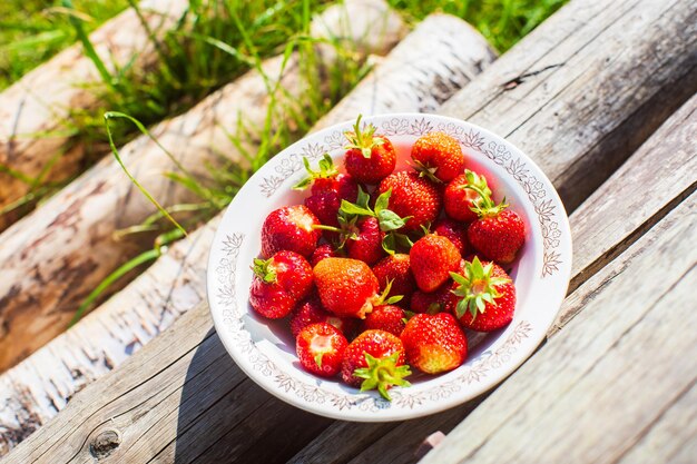 Raccolto di fragole in primo piano sdraiato in un piatto su gradini di legno rurali Il concetto di cibo sano vitamine mercato agricolo vendita di fragole