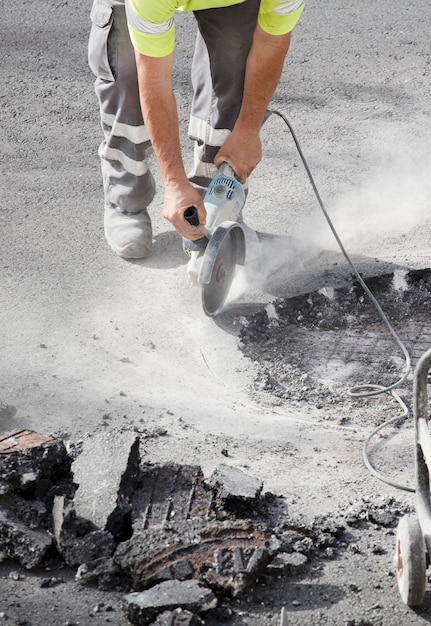 radiale con disco per pietra nelle mani di un operatore in uniforme che taglia il terreno di asfalto, polvere i