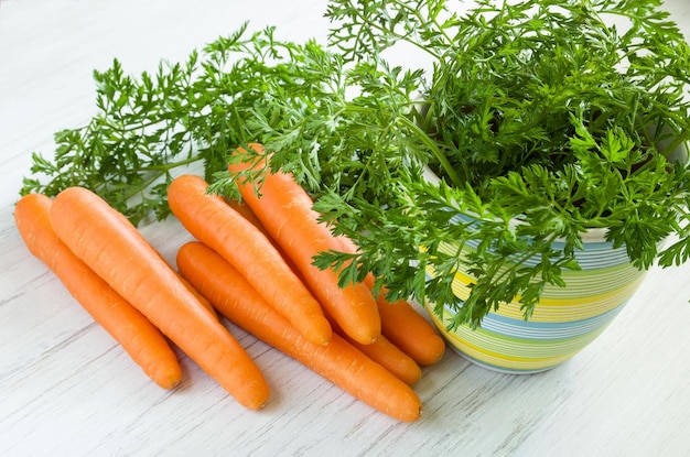 Radice di carota con foglie in vaso di ceramica su sfondo bianco tavolo in legno