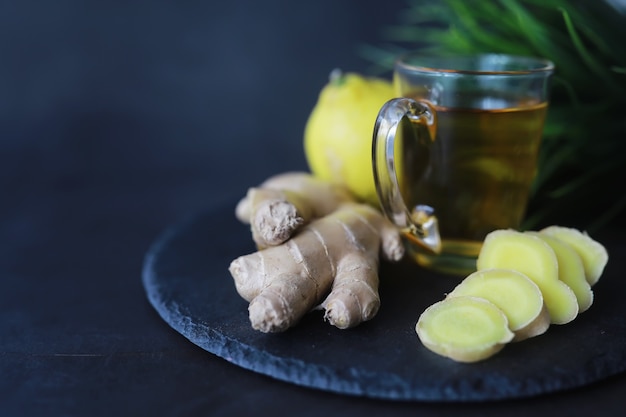 Radice di zenzero intera e affettata. Tè allo zenzero con limone sullo sfondo scuro. Radice di zenzero fresco su sfondo di pietra. Vitamine. Vista dall'alto. Spazio libero per il tuo testo.