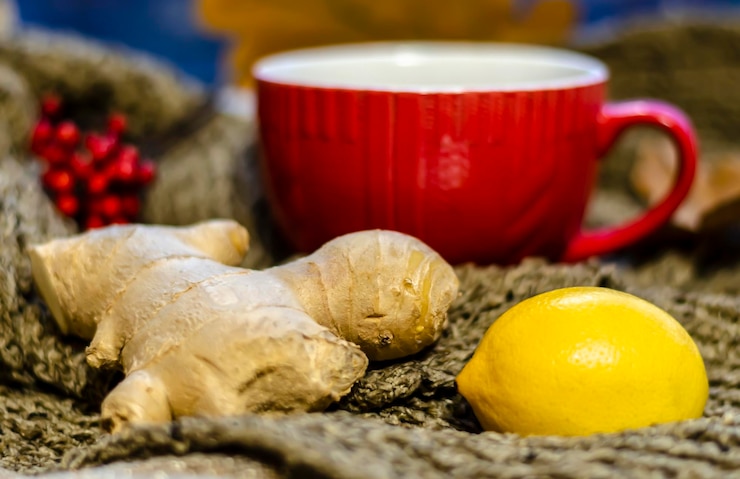 Foto radice gialla di limone e zenzero sullo sfondo di una tazza rossa con tè e bacche di sorbo sfocato fuoco
