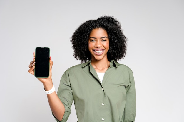 Radiosa di gioia, questa donna afroamericana mostra il suo telefono con lo schermo vuoto.