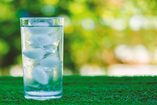 Raffreddare l&#39;acqua in un bicchiere di ghiaccio con sfondo sfocato verde naturale