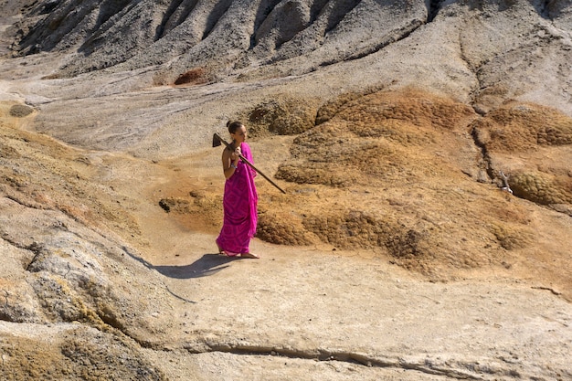 Ragazza a piedi nudi in sari che cammina nel deserto con una zappa sulla spalla