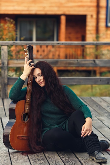 Ragazza abbastanza dai capelli lunghi che si siede sulla natura con la chitarra.