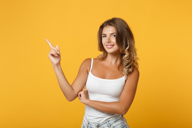 Ragazza abbastanza giovane donna in abiti casual leggeri in posa isolata su sfondo giallo arancio in studio. Persone sincere emozioni concetto di stile di vita. Mock up spazio di copia. Puntando il dito indice da parte verso l'alto.